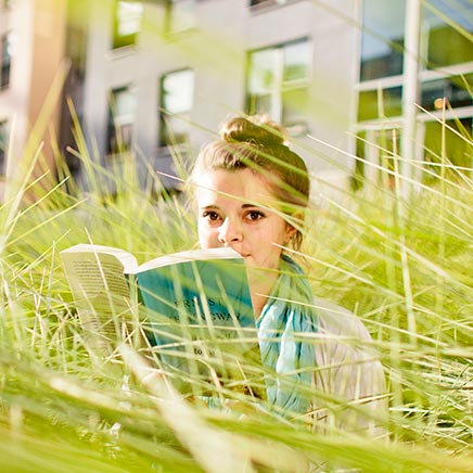 Female student sitting in tall grass reading a book